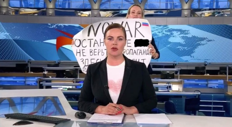 Марина Овсянникова (на заднем плане) с плакатом в студии Первого канала