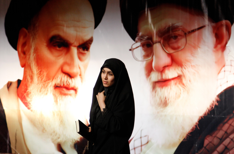Иранская женщина проходит мимо плаката с изображением Рухоллы и Али Хомейни