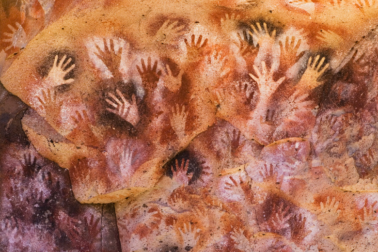 Перекрывающиеся силуэты ладоней, обведенных охрой — частый сюжет пещерной живописи. Мы пока не знаем, что он означает. Фото: Shutterstock