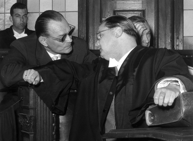 Бывший глава полиции Мемеля (Клайпеды), оберфюрер СС Бернгард Фишер-Шведер (в темных очках) консультируется со своим адвокатом на судебном процессе над айнзатцгруппами в Ульме (1958)