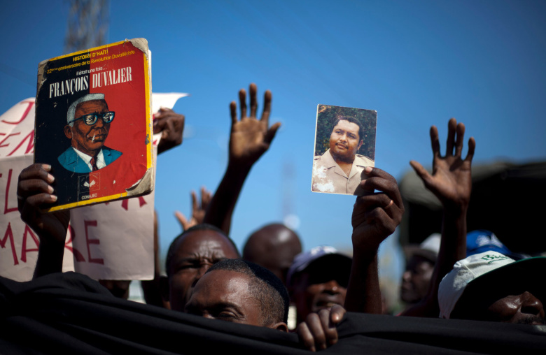 Гаитяне на митинге держат изображения Франсуа (слева) и Жан-Клода Дювалье (справа), 2011 год