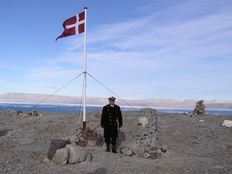 Командир фрегата HDMS Triton Королевских военно-морских сил Дании Пер Старклинт на острове Ханс возле датского флага в августе 2003 года