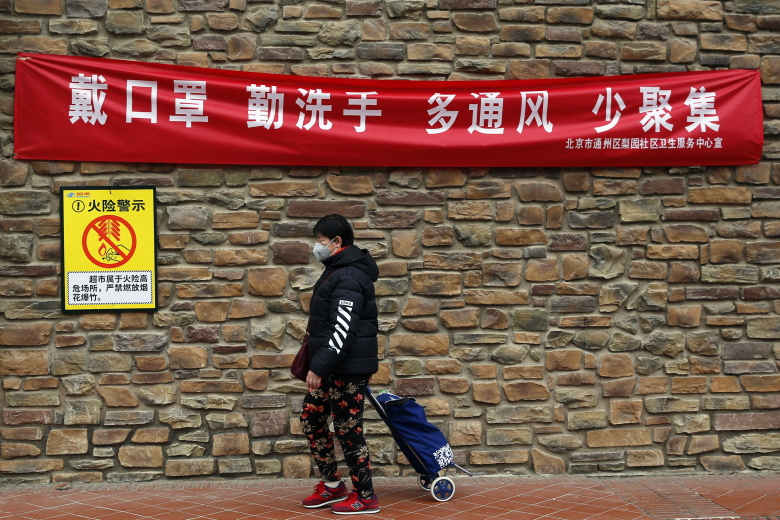 Прохожий идет у плаката "Носите маски. Тщательно мойте руки. Чаще проветривайте помещение. Меньше контактируйте друг с другом", Пекин, Китай. Фото: Wu Hong / EPA / TASS