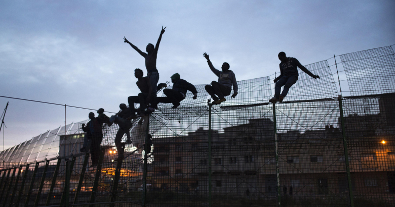 Мигранты карабкаются через забор между Морокко и испанской Мелильей.