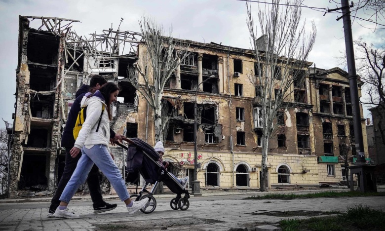 Семья проходит мимо разрушенного дома в Мариуполе