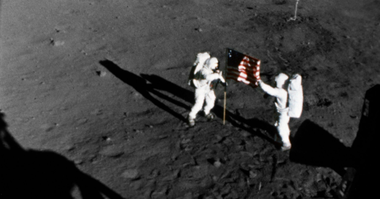 Нил Армстронг (слева) и Базз Олдрин устанавливают флаг США. Кадр, снятый 16-мм кинокамерой лунного модуля