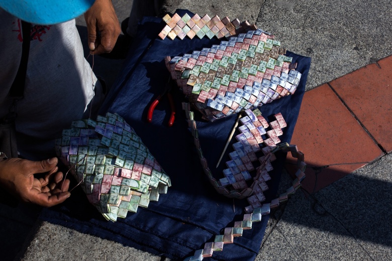 Уличный торговец делает поделки из боливаров. Фото: Wil Riera / Bloomberg / Getty Images